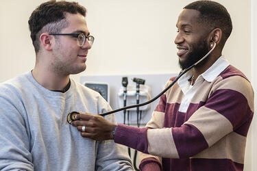 Clinician faces a patient while listening to their heart with a stethoscope