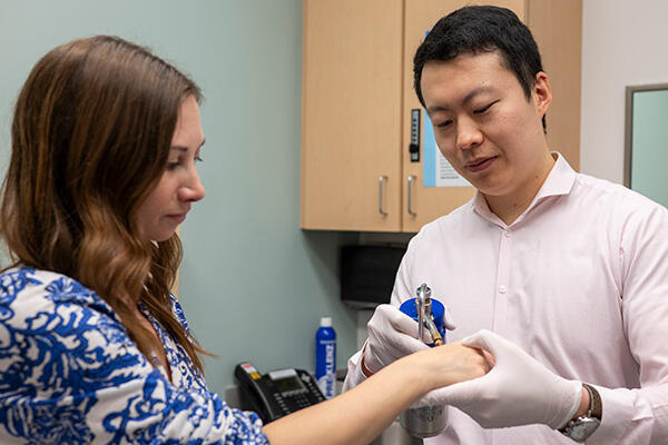 A dermatologist holds a patient’s arm while examining the skin on their wrist with a clinical tool